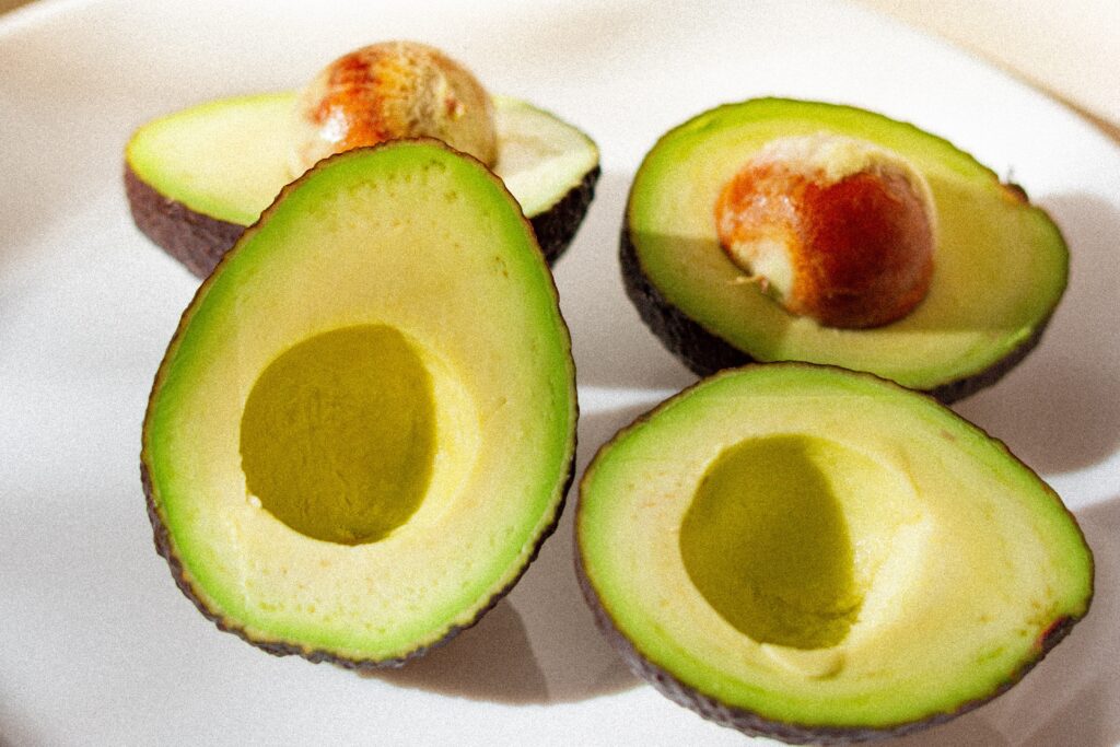 Avocados kept on a plate, two with pits and two without pits. 
Avocados are harmful for the pet dogs.
